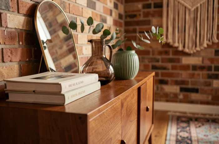 Vignette décorative tendance sur un buffet scandinave avec carafe en verre fumé, céramique sauge et miroir laiton courbé